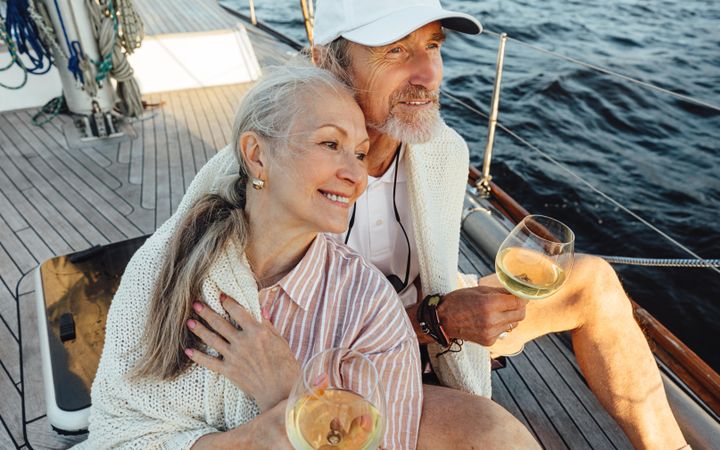 Happy older couple sitting on a boat with wine in hand