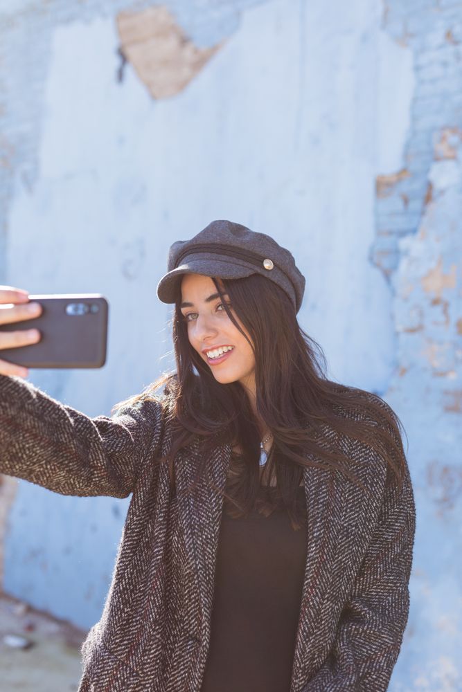 Charming Hispanic woman taking selfie near wall