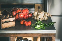 Wire basket of tomatoes, bunch of garlic, basil and spice rack on kitchen counter