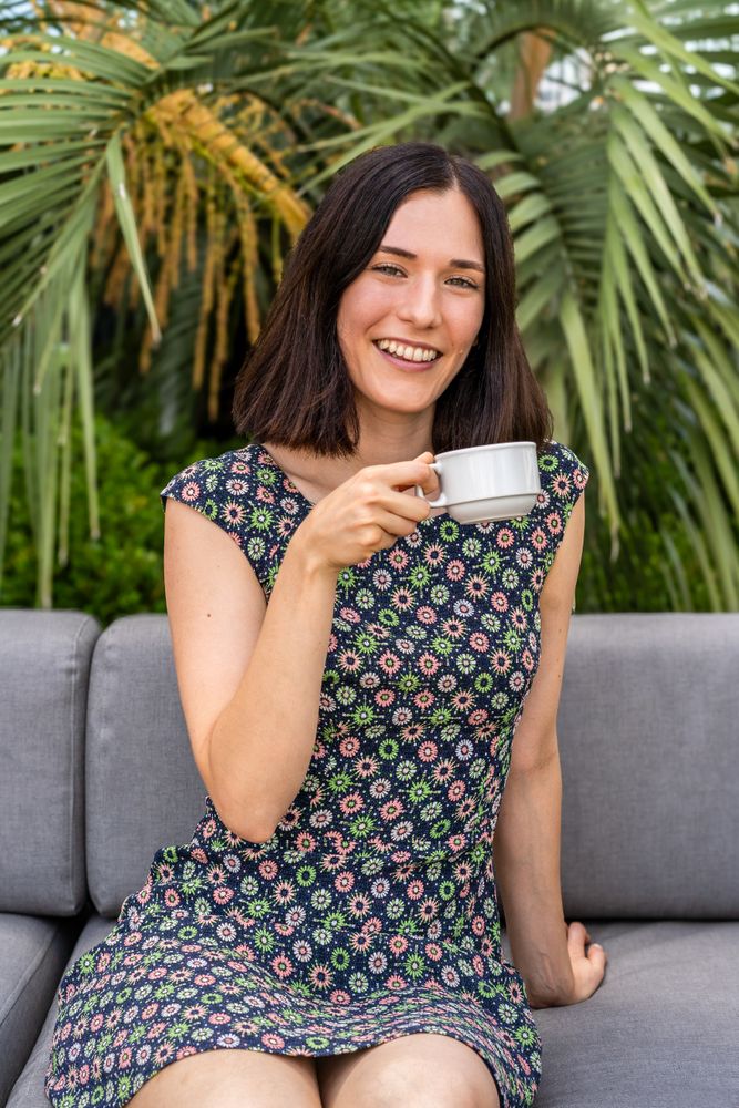 A smling woman is sitting on a couch and holding a cup of coffee