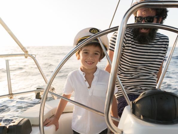Man with boy holding steering wheel on yacht on water