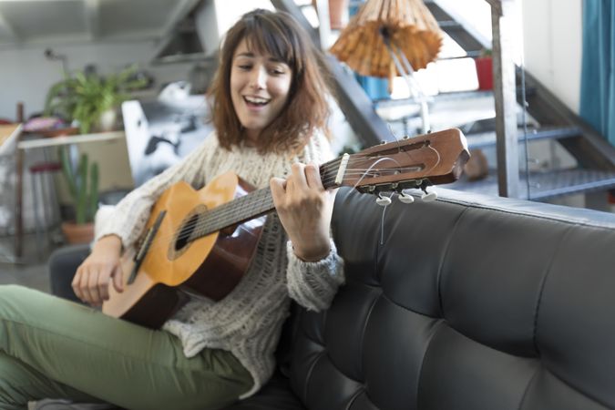 Female on sofa playing acoustic guitar while singing at home
