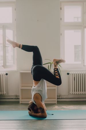 Fit woman practicing yoga pose and standing on head at home