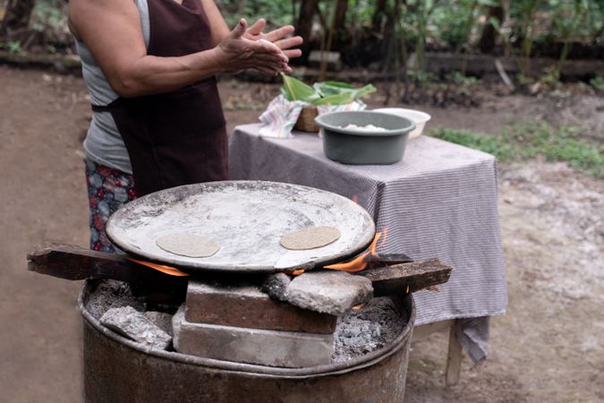 An adult Hispanic woman is shaping corn tortillas by hand