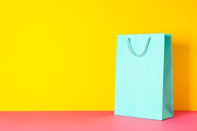 Color paper bag on pink table against yellow background, copy space