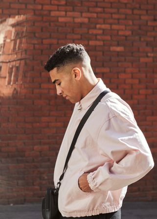 Side view of stylish young man in jacket against a red brick wall