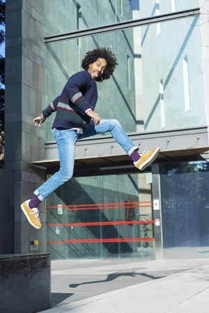 Black man in cardigan taking jumping outdoors in the sun