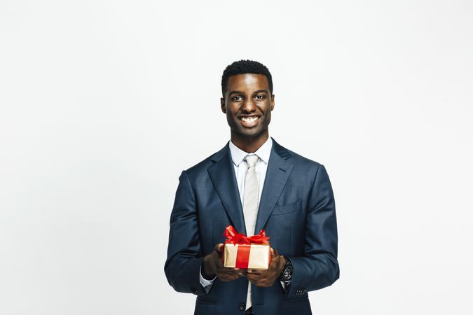 Smiling Black man presenting present wrapped in gold paper with red bow