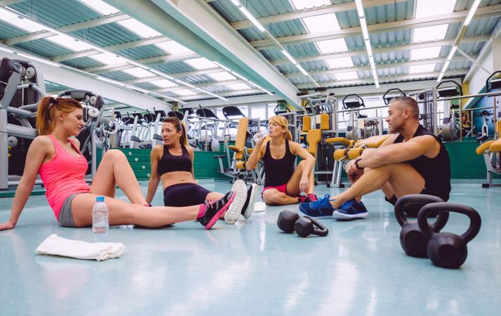 Group of fit people sitting on floor in gym with kettle bells