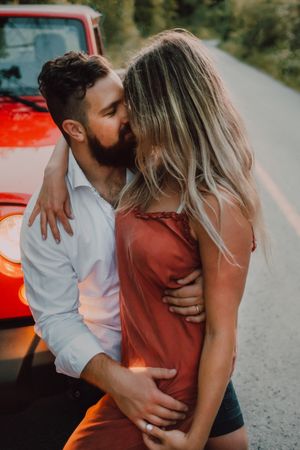Loving couple sitting on car on road near forest