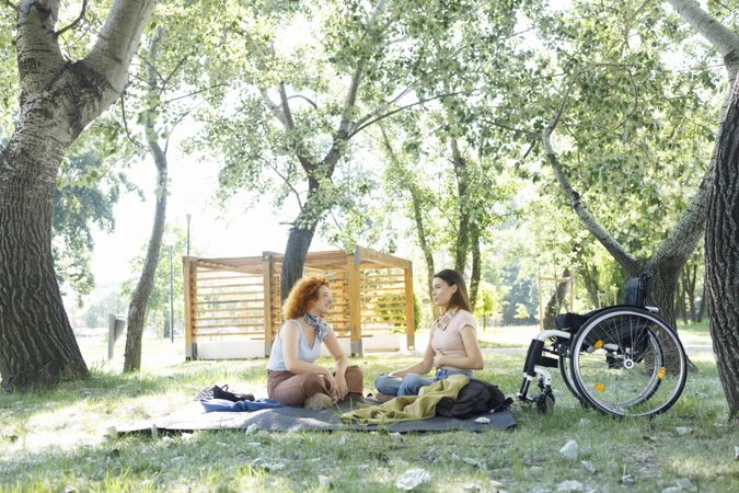 Woman with a disability sitting next to her wheelchair having a picnic with friend