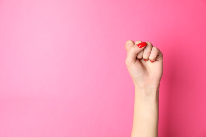 Woman hand with red nails on pink background, space for text