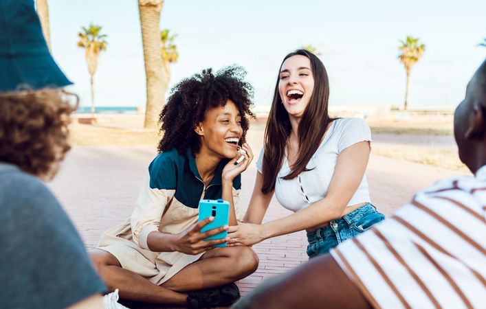 Group of multiethnic young people hanging out outdoors with two women holding smartphone