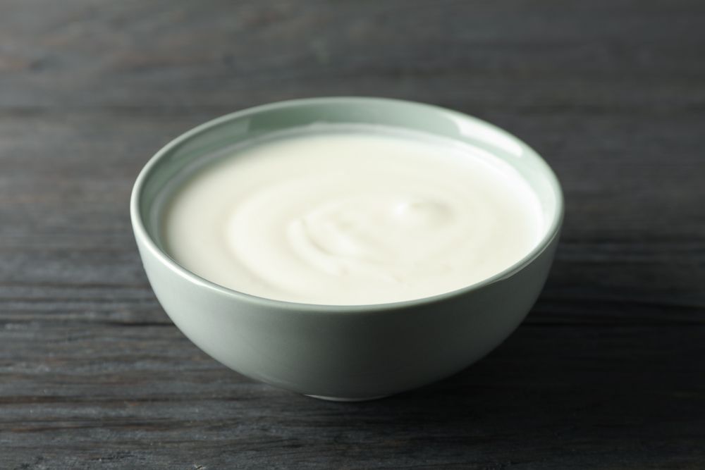 Bowl of sour cream yogurt on dark wooden background