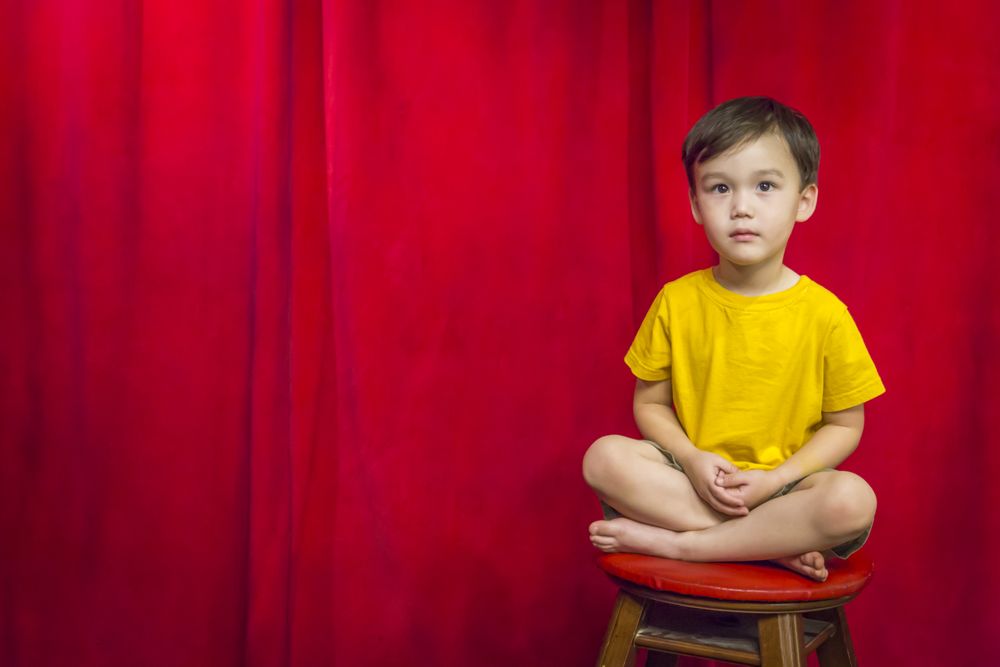 Biracial Boy Sitting on Stool in Front of Curtain