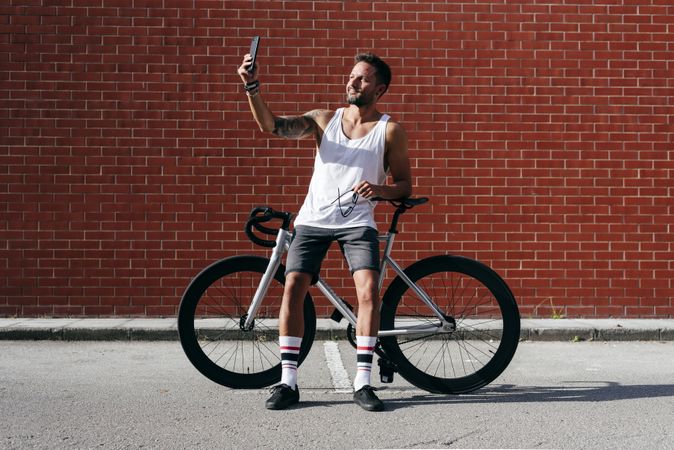 Sportive man with bicycle using phone