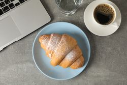 Top view of plate with croissant with water glass and laptop