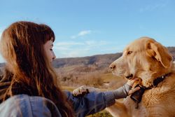 Woman with piercing sitting near dog between field