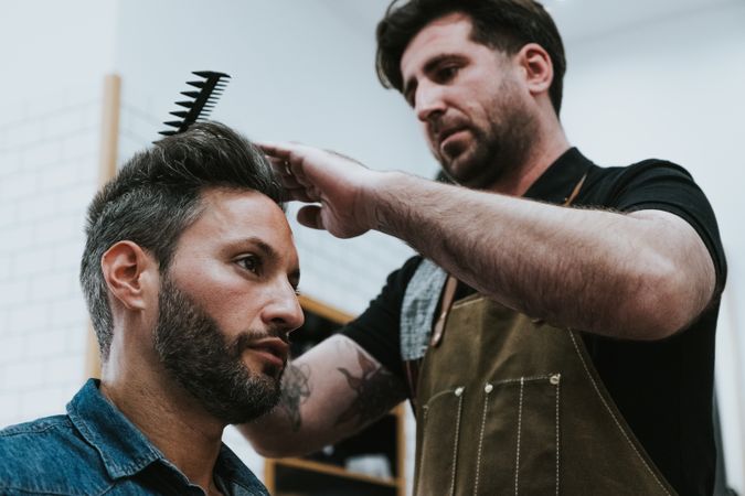Barber combing hair to man in salon