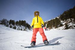 Man in yellow parka and goggles standing on snowboard