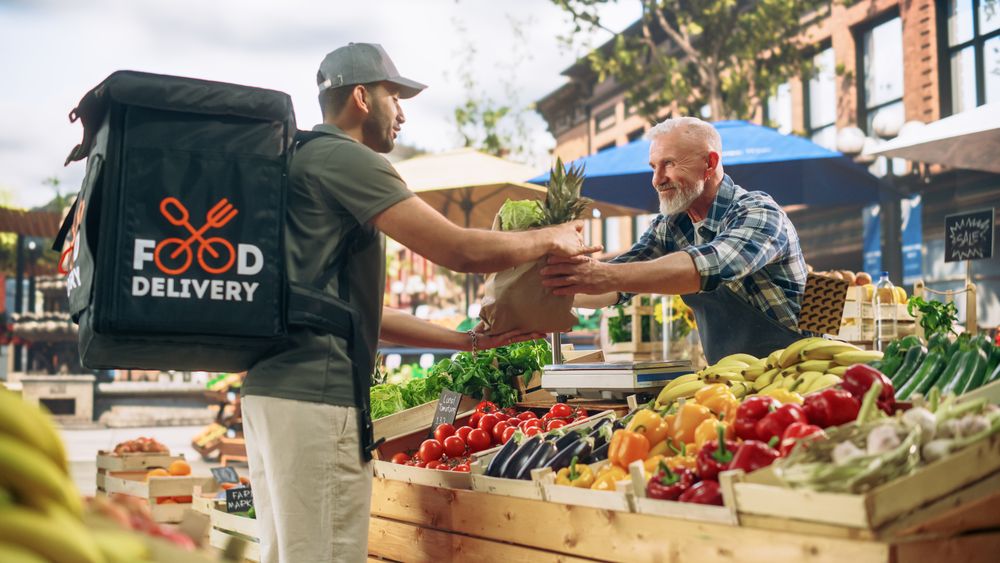 Cheerful Street Vendor Handing Over a Recycled Paper Bag with Fresh Produce