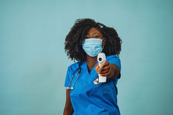 Portrait of Black medical professional in face mask dressed in scrubs with a digital thermometer