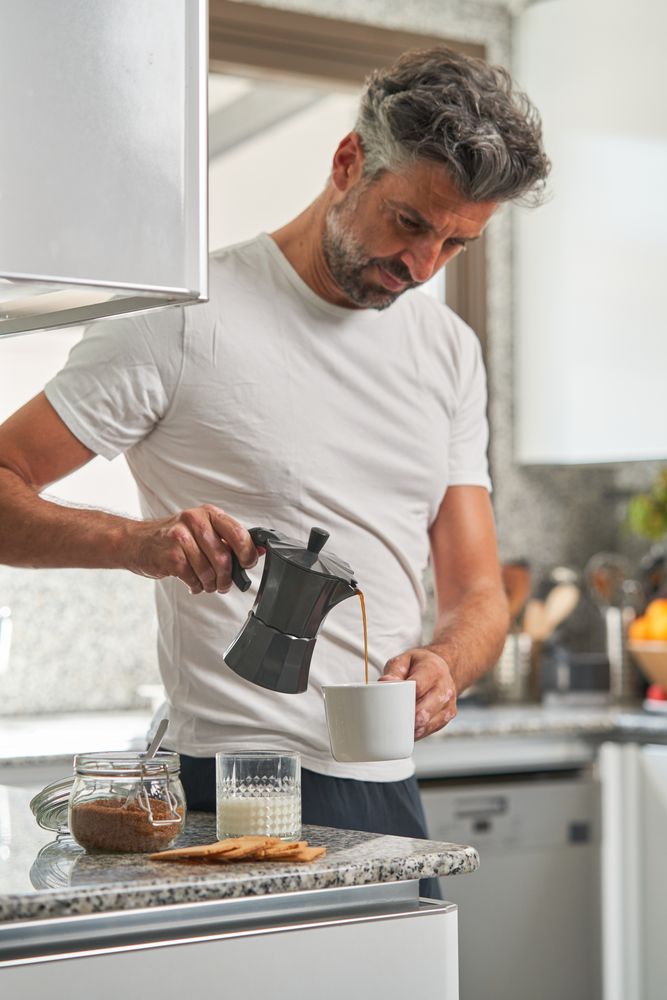 Serious man pouring coffee from moka pot in kitchen