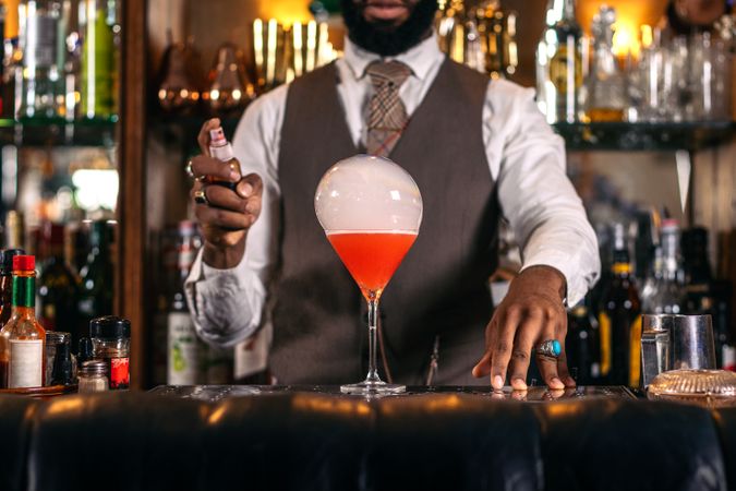 Stylish Black bartender preparing a cocktail with a smoke bubble in a traditional cocktail bar