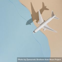 Top view of model airplane with shadow over beige and blue water beach scene 0JEprb