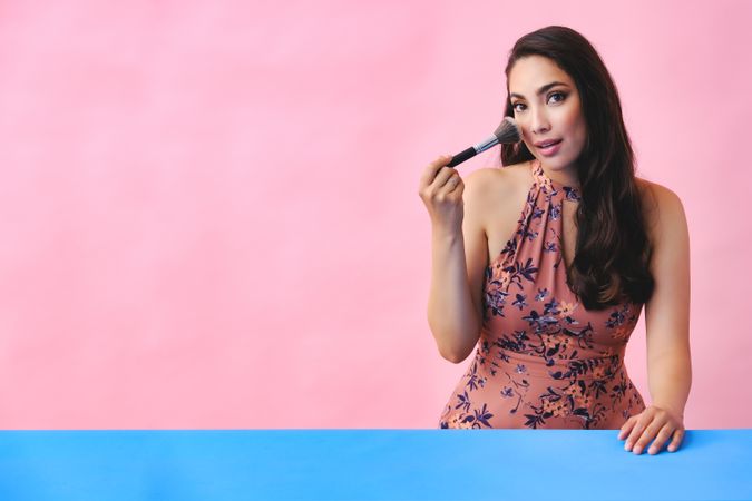 Surprised Hispanic woman with long brown hair holding large make up brush to her face, copy space