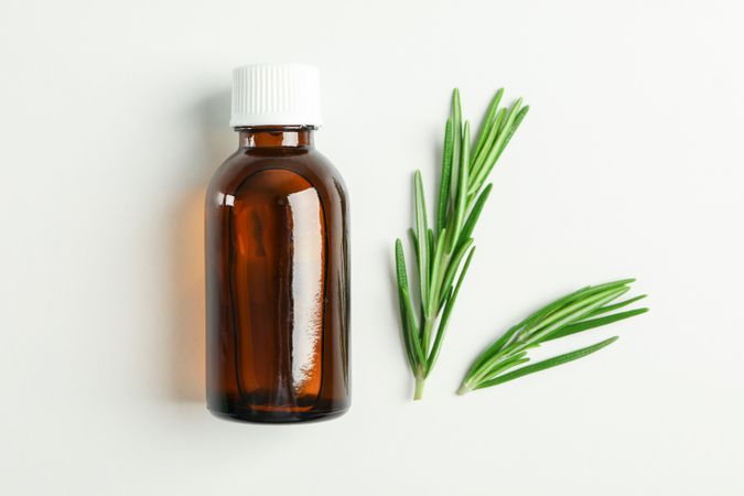 Flat lay composition with rosemary oil and leaves on plain background, space for text