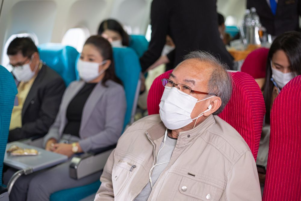 Older male wearing facemark and earbuds in flight