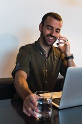 Cheerful man talking on smartphone near laptop