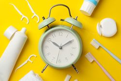 Alarm clock and dental care tools on yellow background, top view