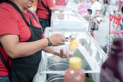 An Hispanic adult woman is serving some vanilla ice cream balls in a cup in the street