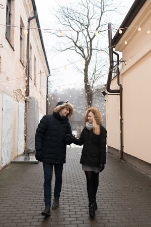 Smiling couple holding hands on street with fairy lights hanging on buildings