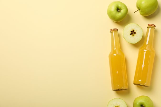 Glass bottles with cider and green apples on beige background, space for text