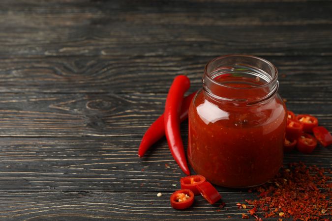 Chilli pepper and glass jar of sauce on wooden  background