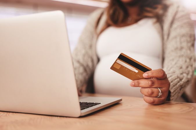 Close up shot of pregnant woman using laptop and holding credit card on table