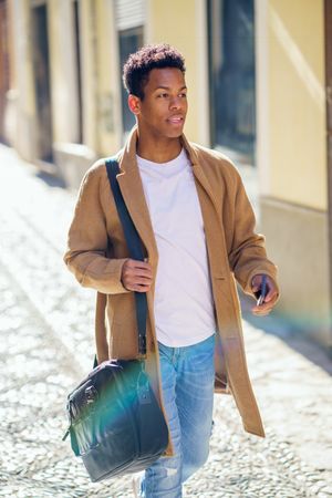 Cuban male strolling down street with leather bag and phone, with rainbow lens flare