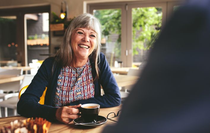 Cheerful woman sitting at table in cafe and talking with a man drinking coffee