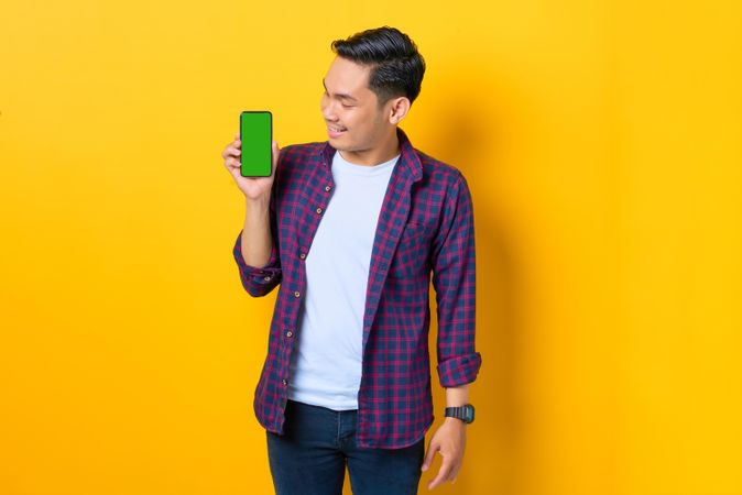 Asian man holding smartphone with chroma key while looking at it