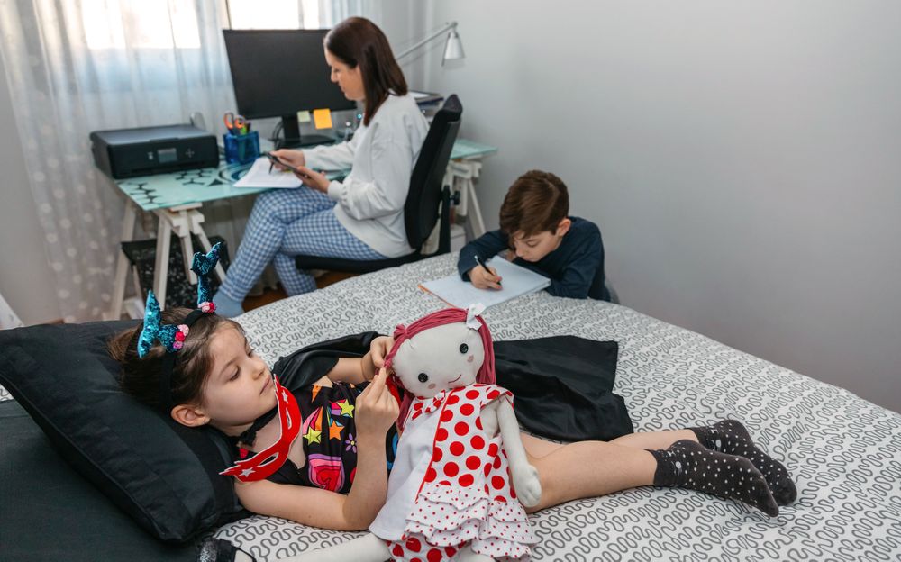 Children playing and doing homework while their mother works at home