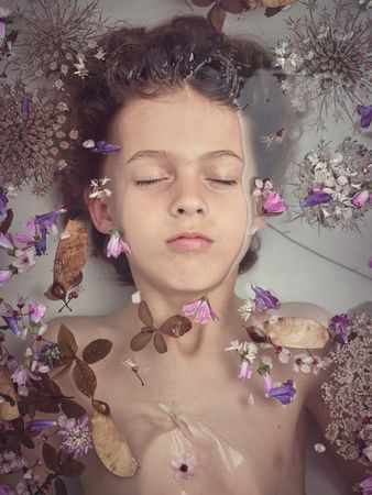Boy lying underwater in bathtub with flowers