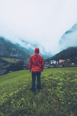 Man in red jacket walking on green grass field near village in Switzerland