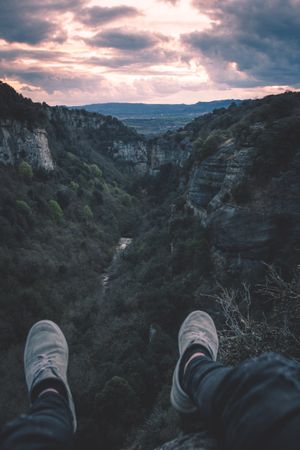 View to small river in canyon and legs of person sitting on the edge
