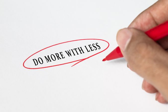 male hand circle do more with less words using red marker on paper.