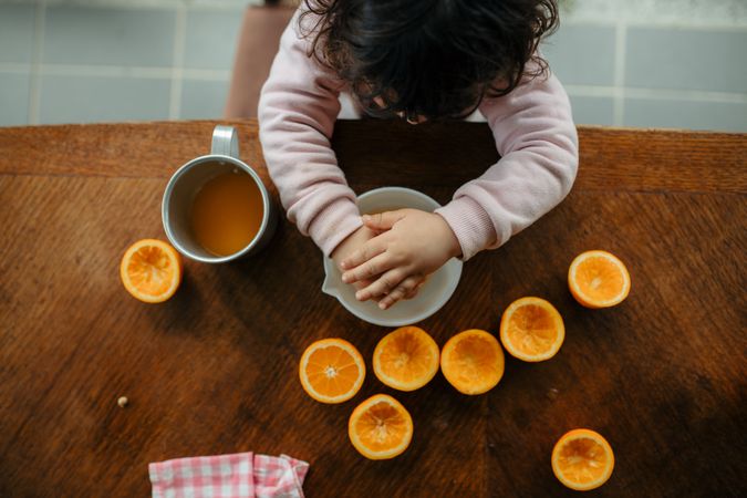 Top view of little girl pressing orange slices to make home made juice