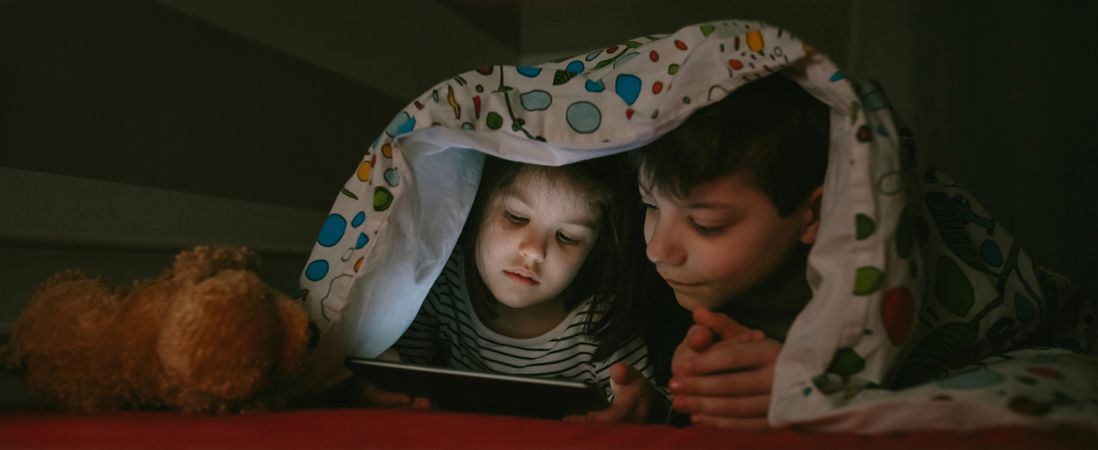 Siblings looking at the tablet in the dark