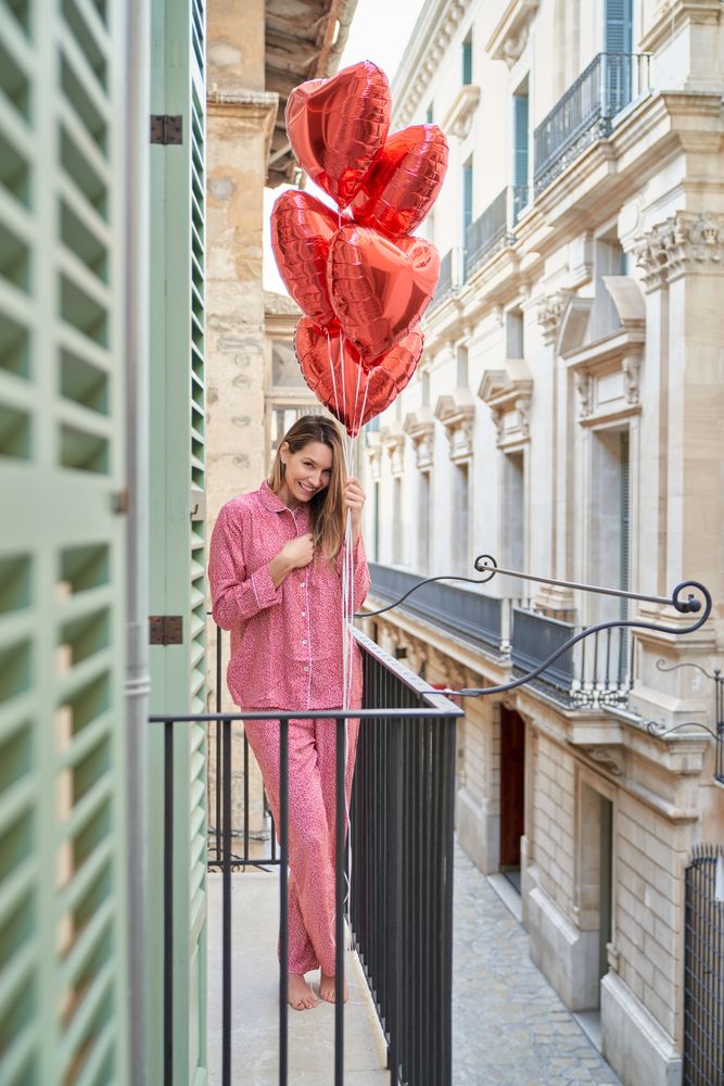 Cheerful woman with bunch of red heart balloons on balcony